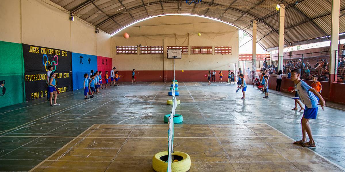 Ginásio dividida em diversas mini quadras, uma extensa rede sustentada por estruturas de pneus e canos PVC separa o espaço ao meio.