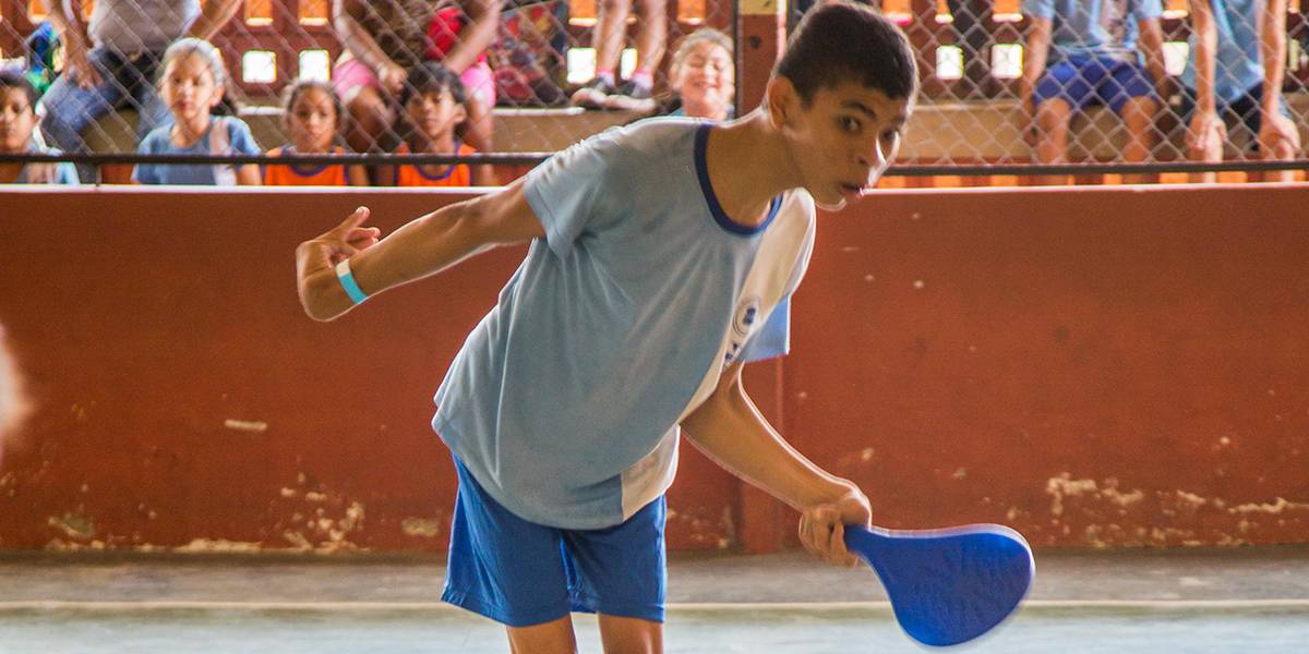 Menino com deficiência física joga tênis com colega.