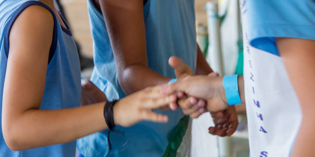 Três meninos sorriem entre si e se cumprimentam com as mãos sobre a rede no meio da quadra.