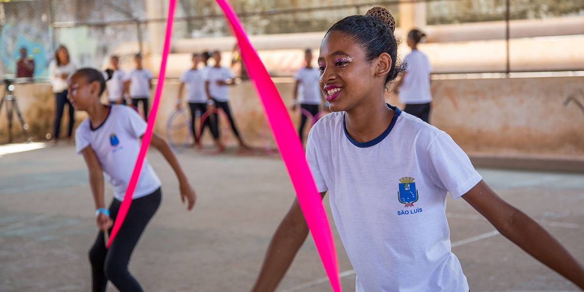 Garota sorridente faz coreografia movimentando uma fita rosa no ar.