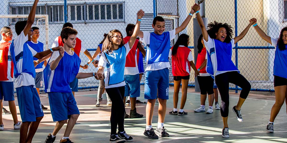 Cinco adolescentes usando coletes azuis e de mãos dadas em linha comemoram. 
