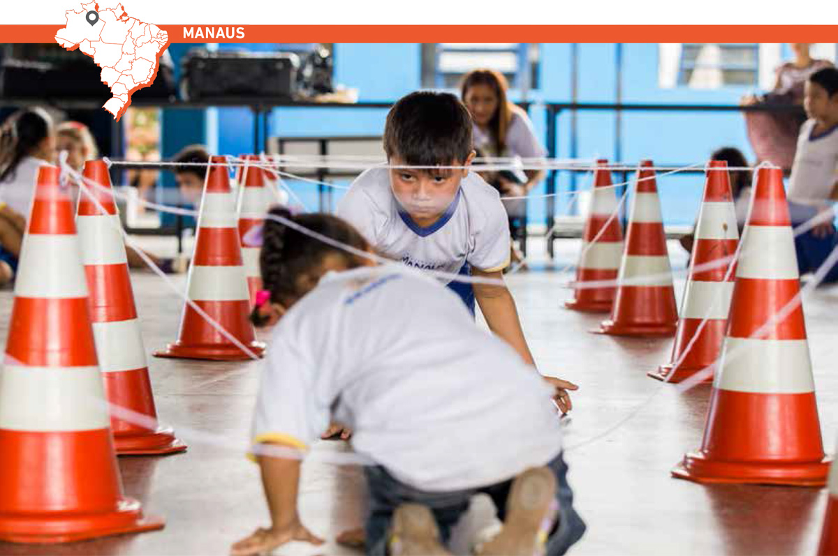 Menino e menina engatinham em sentidos opostos sob uma trama de barbantes amarrados no topo de cones.