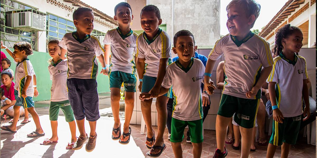 Cinco meninos de mãos dadas em uma fileira pulam juntos e sorriem.